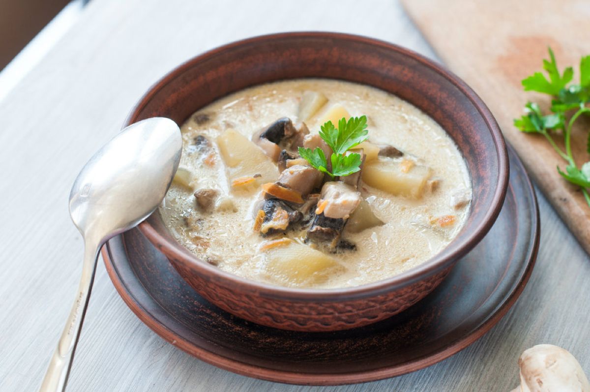 ciotola su piatto piano piena di zuppa patate e funghi, un cucchiaio