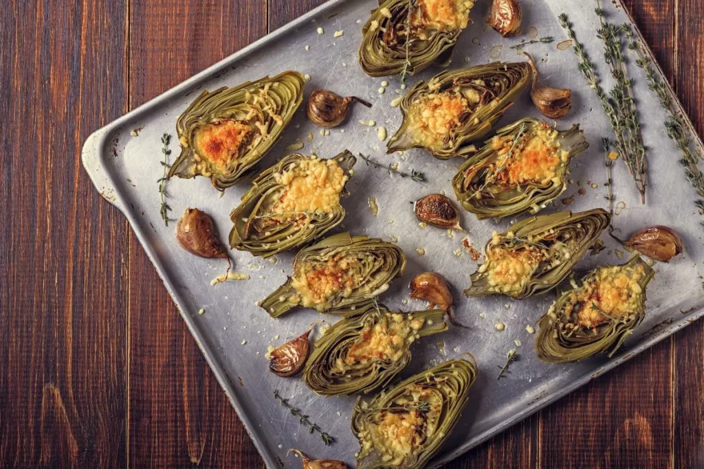 Carciofi ripieni senza carne al forno e in padella 1 su tavolo da cucina, teglia da forno con vari carciofi ripieni con erbe aromatiche