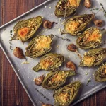 su tavolo da cucina, teglia da forno con vari carciofi ripieni con erbe aromatiche