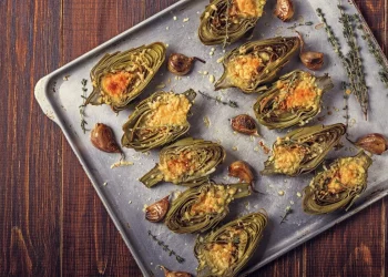 su tavolo da cucina, teglia da forno con vari carciofi ripieni con erbe aromatiche