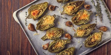 su tavolo da cucina, teglia da forno con vari carciofi ripieni con erbe aromatiche