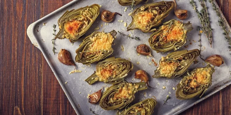 su tavolo da cucina, teglia da forno con vari carciofi ripieni con erbe aromatiche