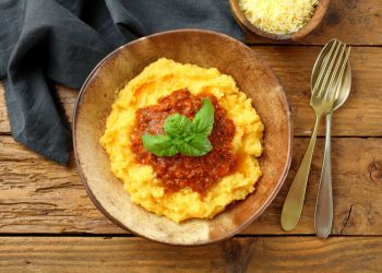su base di legno un piatto di legno colmo di polenta con il sugo