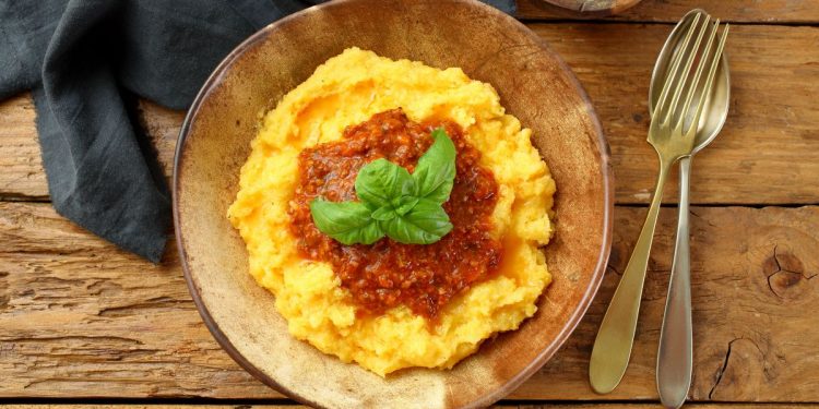 su base di legno un piatto di legno colmo di polenta con il sugo