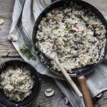 una padella con manico e una ciotola scura piene di risotto ai funghi