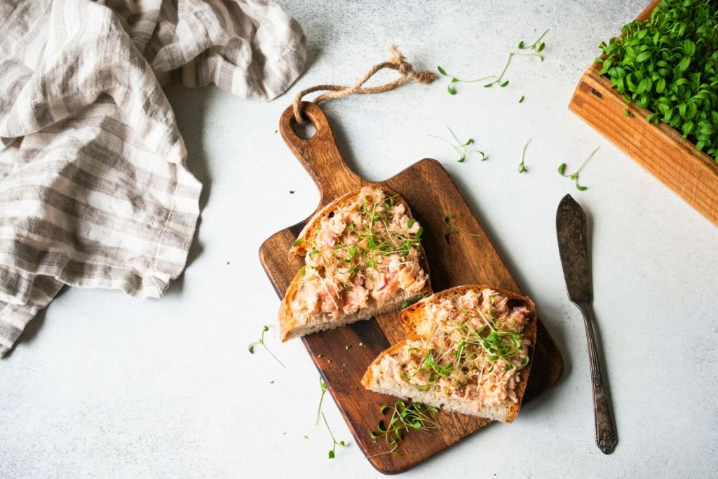 Mousse di salmone, l'antipasto perfetto per una cena gustosa 3 su tavolo di marmo, tagliere con 2 tartine di mousse di salmone, un coltello, un canovaccio e prezzemolo tritato