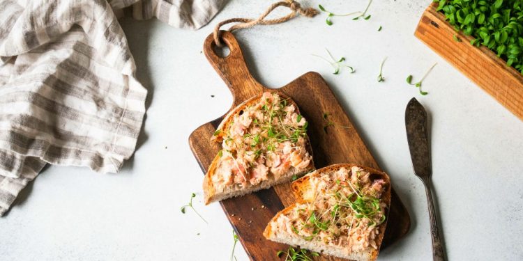 su tavolo di marmo, tagliere con 2 tartine di mousse di salmone, un coltello, un canovaccio e prezzemolo tritato