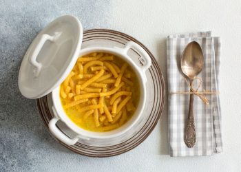 su tavolo di marmo . piatto di argento con una zuppiera che contiene i passatelli in brodo . Sulla destra un tovagliolo di cottone con un cucchiaio legato con un filo con carta