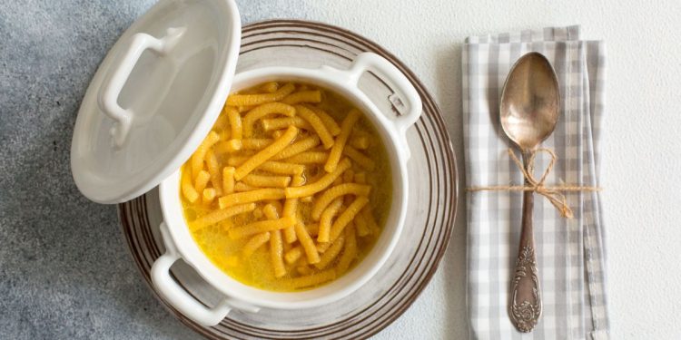 su tavolo di marmo . piatto di argento con una zuppiera che contiene i passatelli in brodo . Sulla destra un tovagliolo di cottone con un cucchiaio legato con un filo con carta