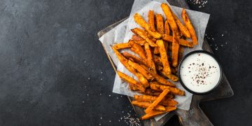 bastoncini di patate dolci fritte su un tavolo con accanto una ciotolina con della salsa