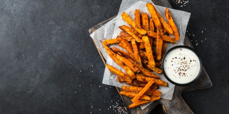 bastoncini di patate dolci fritte su un tavolo con accanto una ciotolina con della salsa
