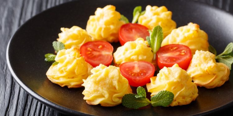 su tavolo di legno, piatto nero con patate duchessa messe in cerchio con attorno pomodorini tagliati e menta