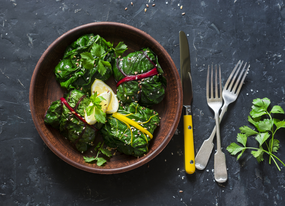 bietola in padella servito in un piatto marrone rotondo, con forchette e coltello accanto