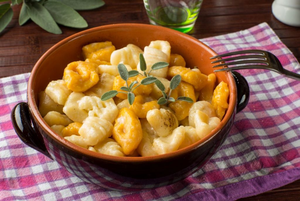 in primo piano su un tavolo con una tovaglia rustica, una cocotte di terracotta con i gnocchi di zucca e ricotta.