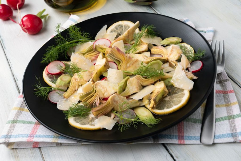 su tavola apparecchiata piatto tondo nero con Insalata di carciofi