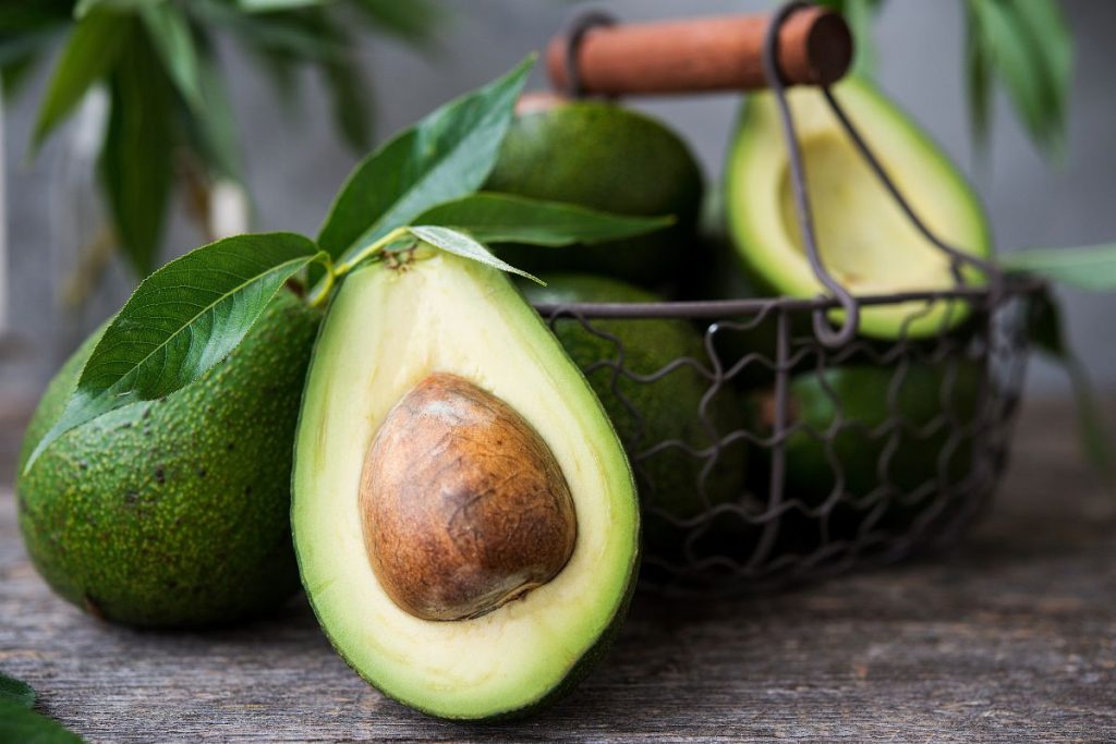 mangiare un avocado al giorno: un cestello con alcuni avocado verdi, un avocado tagliato a metà in primo piano