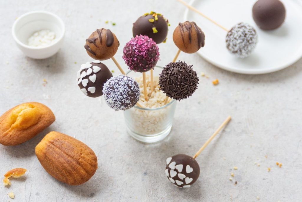 bicchiere di vetro con 7 bastoncini di cake pops di diversi gusti e colori