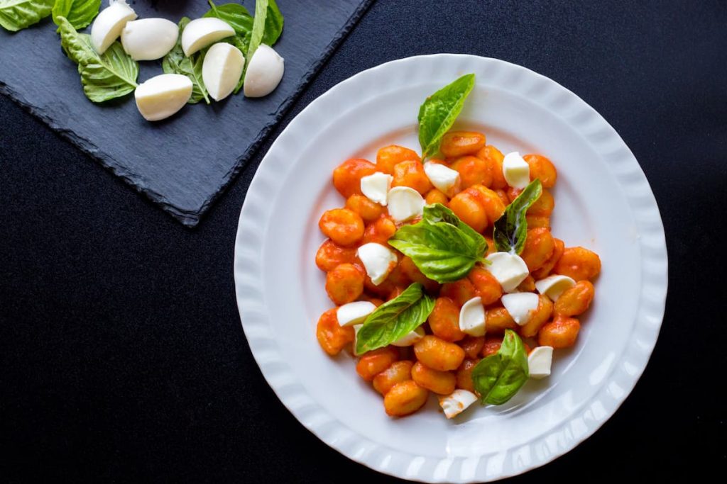 Gnocchi alla Sorrentina, un primo piatto delizioso con pomodoro e mozzarella 3 su sfondo nero, un piatto bianco con gli gnocchi alla Sorrentina con salsa di pomodori e mozzarella