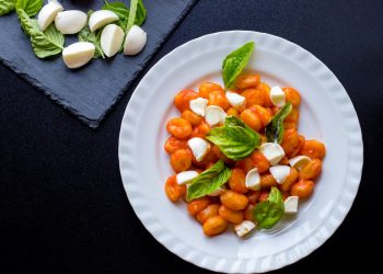 su sfondo nero, un piatto bianco con gli gnocchi alla Sorrentina con salsa di pomodori e mozzarella