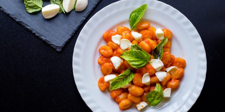 su sfondo nero, un piatto bianco con gli gnocchi alla Sorrentina con salsa di pomodori e mozzarella