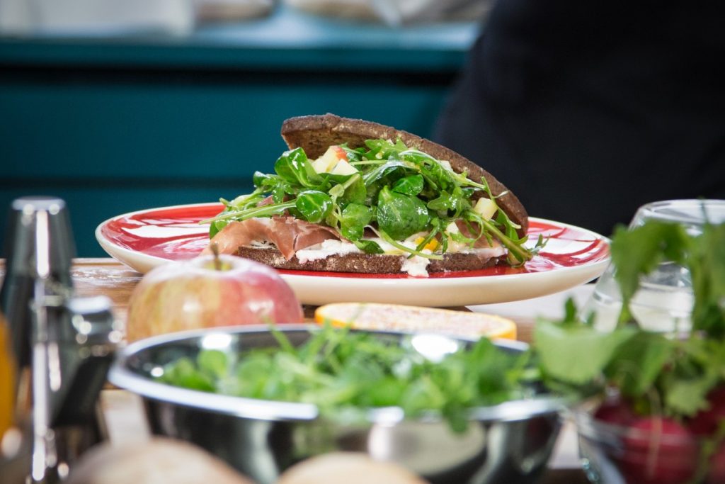 su tavola apparecchiata un piatto con al centro un panino integrale con prosciutto crudo e insalata