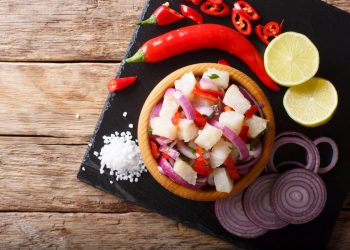 vassoio bero quadrato con ciotola di ceviche, fette di cipolla, spicchi di limone e peperoncini