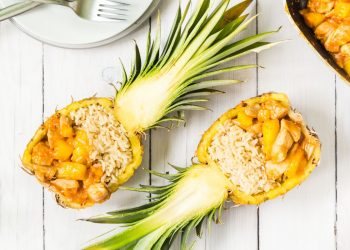 su base di legno chiaro due metà di un ananas ripiene di riso e bocconcini di pollo