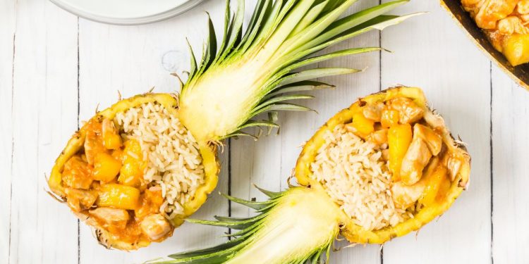 su base di legno chiaro due metà di un ananas ripiene di riso e bocconcini di pollo
