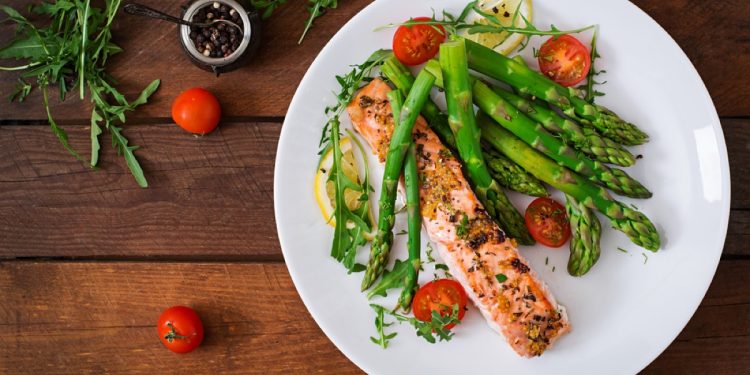 piatto su tavola di legno con trancio di salmone, asparagi e pomodorini