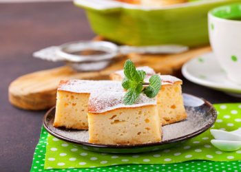 su tavolo apparecchiato per la colazione sotto piatto verde a pois bianco con un piatto nero e torta alla ricotta con un foglio di menta. accanto una tazza di tè