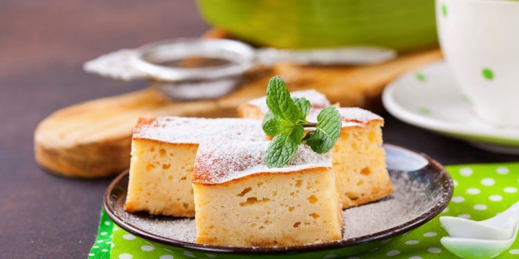 su tavolo apparecchiato per la colazione sotto piatto verde a pois bianco con un piatto nero e torta alla ricotta con un foglio di menta. accanto una tazza di tè