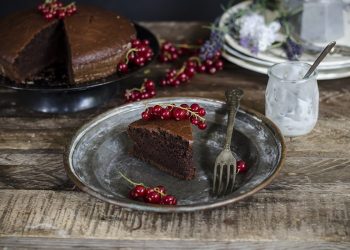 su base neutra, un piatto tondo di metallo con una porzione di torta al cacao e yogurt con dei ribes