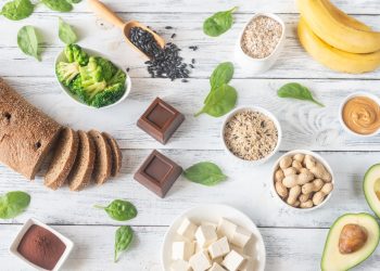 su tavolo di legno bianco alimenti ricchi di magnesio come pane integrale cioccolato fondente, banana e avocado