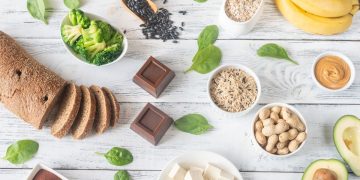 su tavolo di legno bianco alimenti ricchi di magnesio come pane integrale cioccolato fondente, banana e avocado