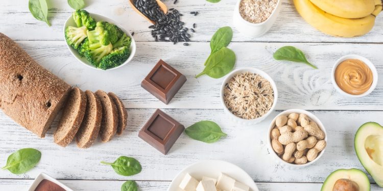 su tavolo di legno bianco alimenti ricchi di magnesio come pane integrale cioccolato fondente, banana e avocado