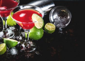 due calici con cocktail rosso Sosmolitan, fettine di lime e spicchi
