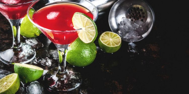 due calici con cocktail rosso Sosmolitan, fettine di lime e spicchi