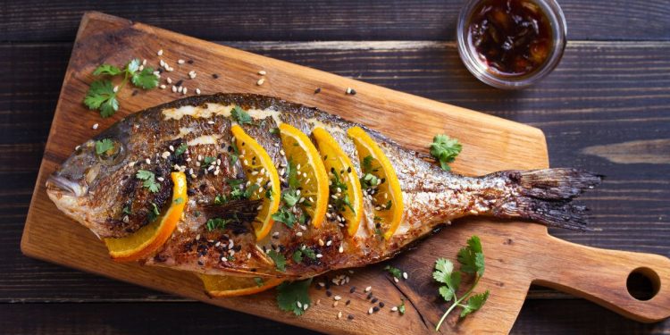 vassoio di legno con una orata al forno e fette di arancia