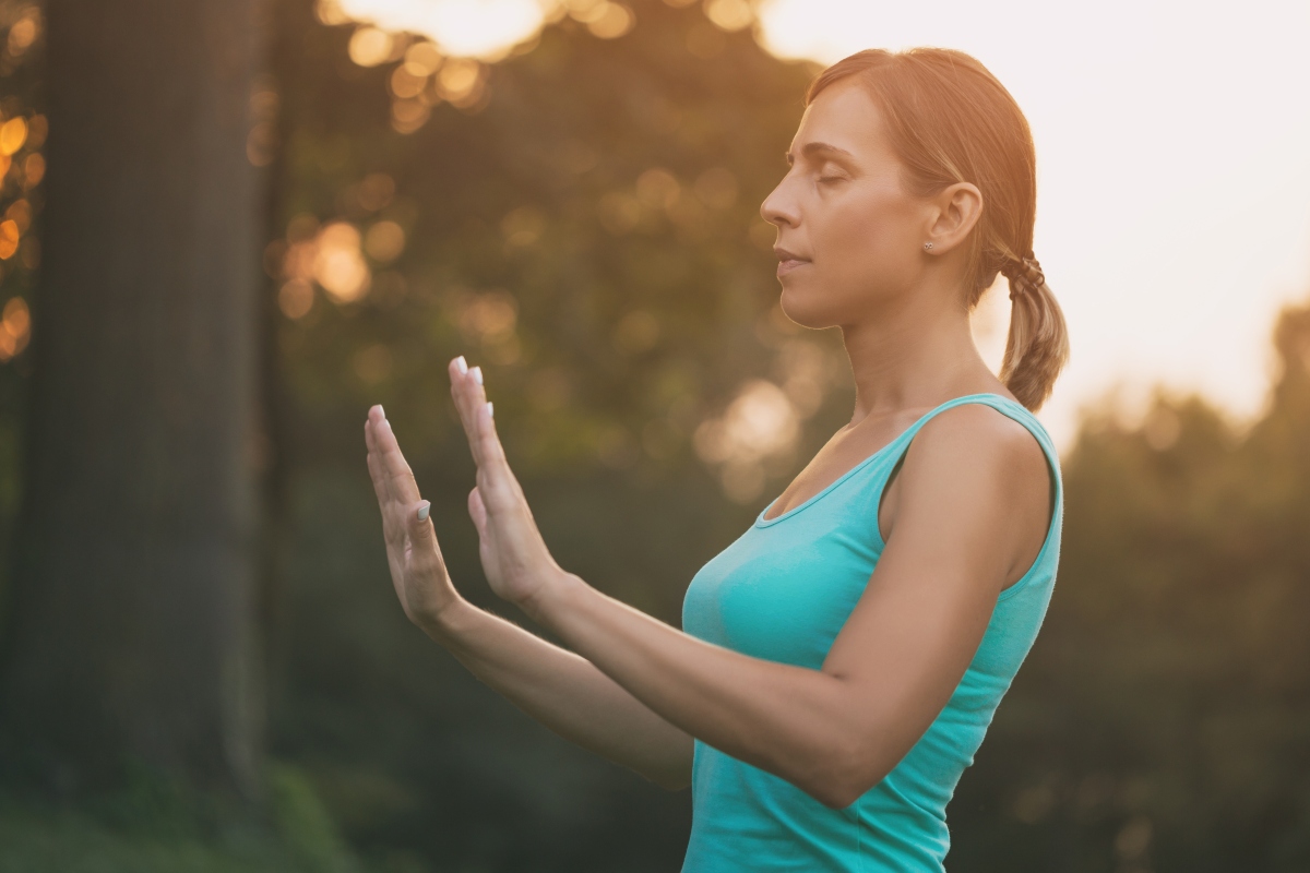 una donna con maglietta verde pratica il tai chi in un bosco occhi chiusi