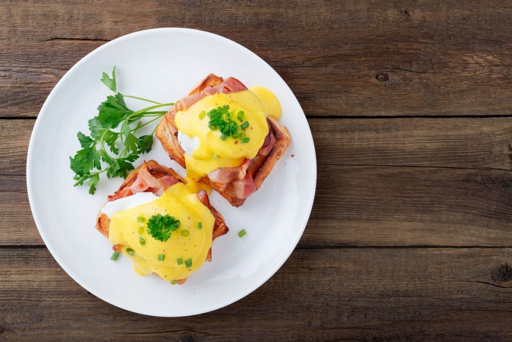 Uova alla Benedict, un goloso piatto americano per la tua colazione 2 su base di legno un piatto tondo bianco con sopra due uova alla Benedict