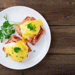 su base di legno un piatto tondo bianco con sopra due uova alla Benedict