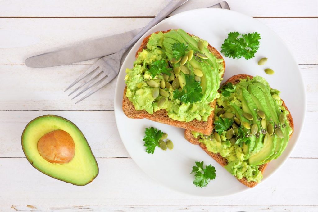su base di legno chiaro mezzo avocado e un piatto bianco con due avocado toast