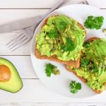 su base di legno chiaro mezzo avocado e un piatto bianco con due avocado toast