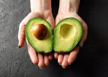 Avocado fa ingrassare? Due mani femminili che tengono le due parti di un avocado aperto a metà