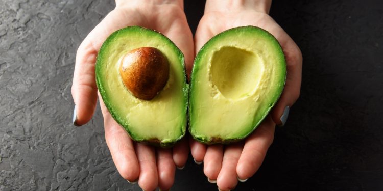 Avocado fa ingrassare? Due mani femminili che tengono le due parti di un avocado aperto a metà