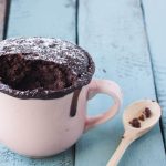 su base di legno celeste una tazza rosa con dentro la mug cake e un cucchiaino