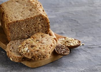 un pane su base di legno e due fette, mestoli con semi di cereali