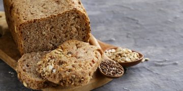 un pane su base di legno e due fette, mestoli con semi di cereali