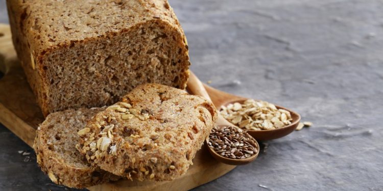 un pane su base di legno e due fette, mestoli con semi di cereali