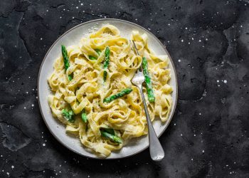 su sfondo nero un piatto bianco con pasta con asparagi croccanti e cremosi